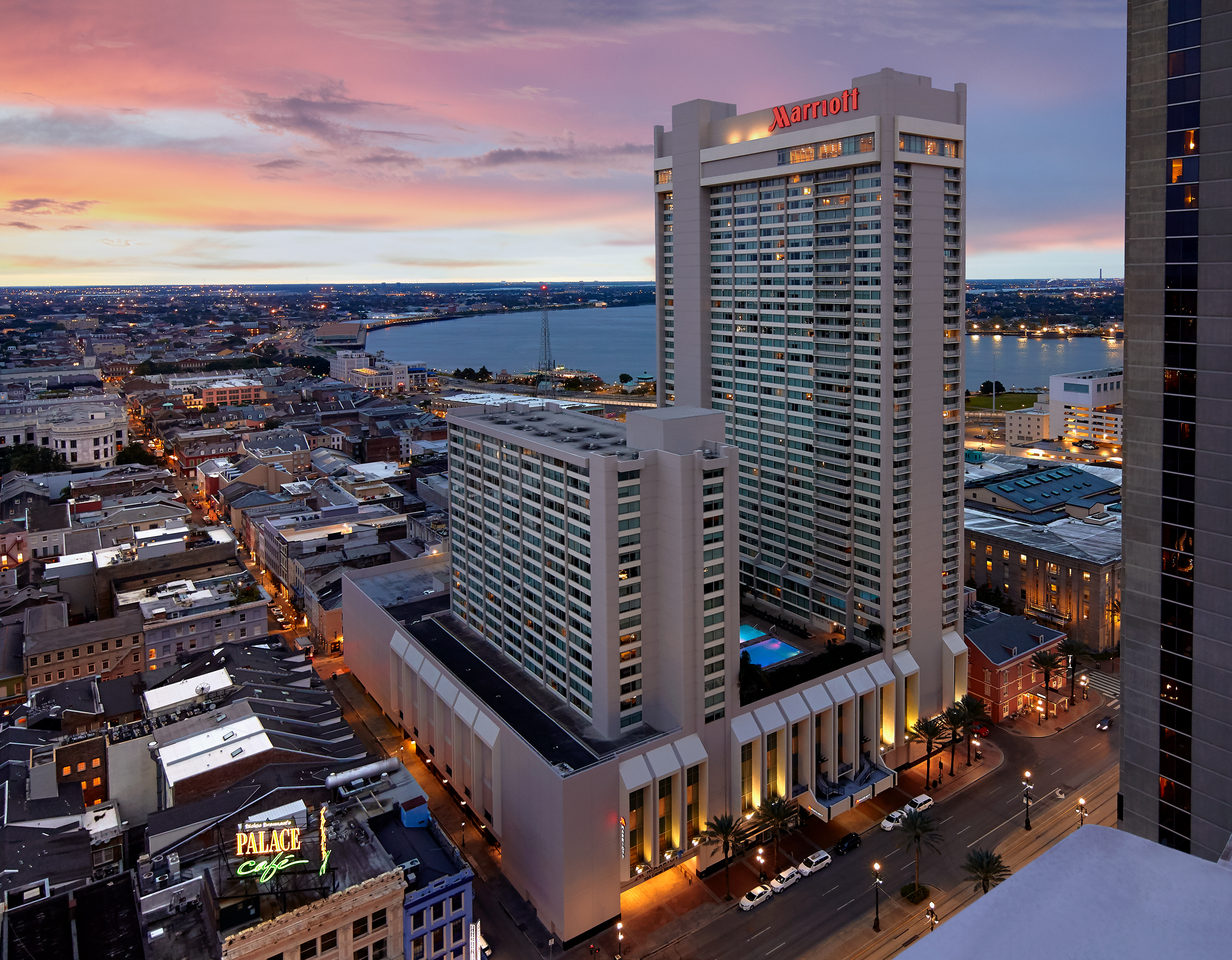 A photo of the Marriott in New Orleans, a tall building with smaller city buildings and a sunset behind it.