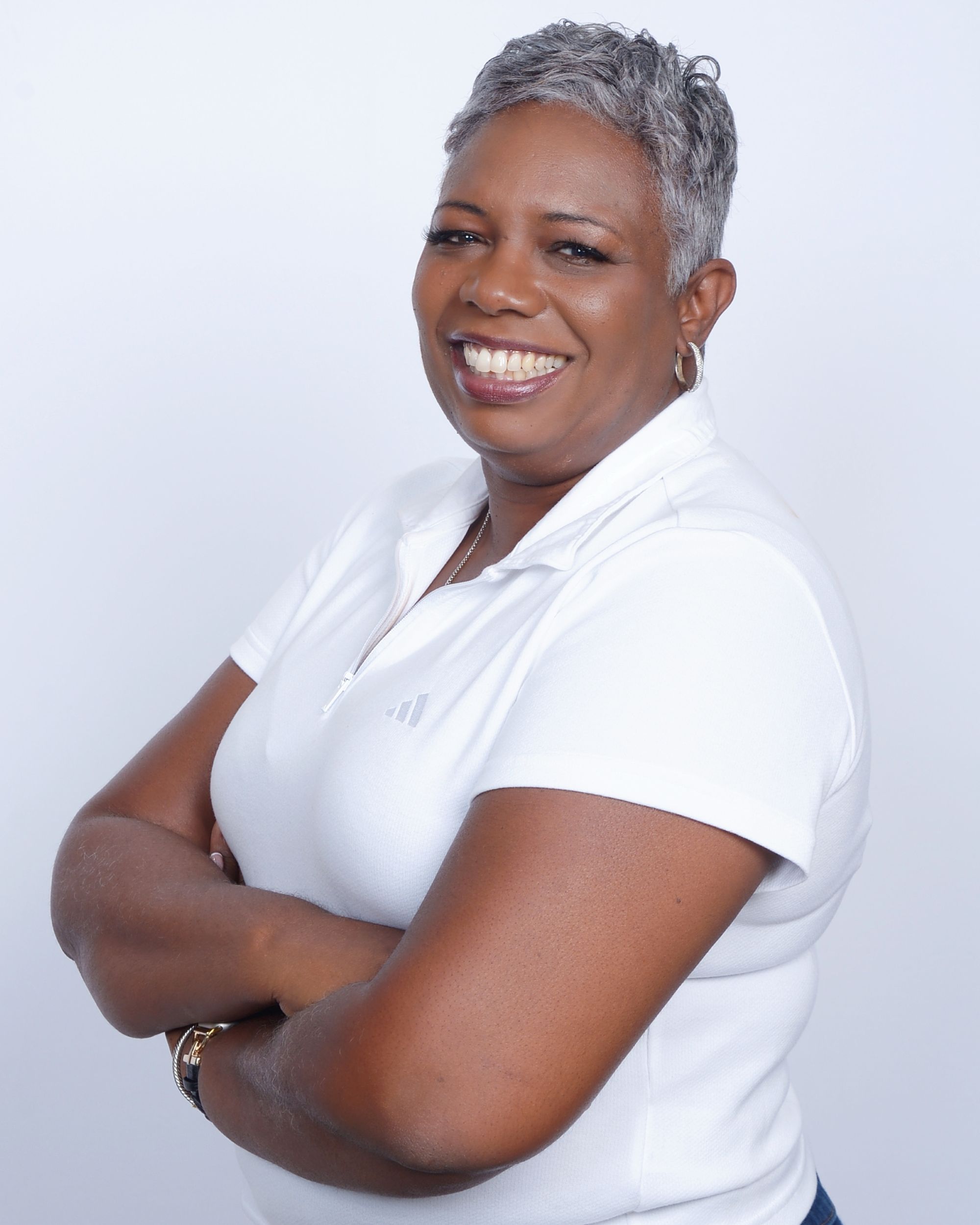 Keisha Bishop stands with her arms crossed, smiling at the camera, wearing a white polo.