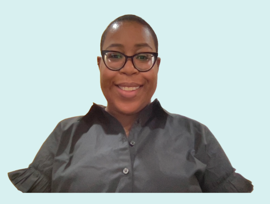 A woman with black frame glasses is smiling while sitting in front of a light blue background.