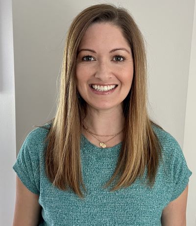 A woman smiling while standing in front of white wall.